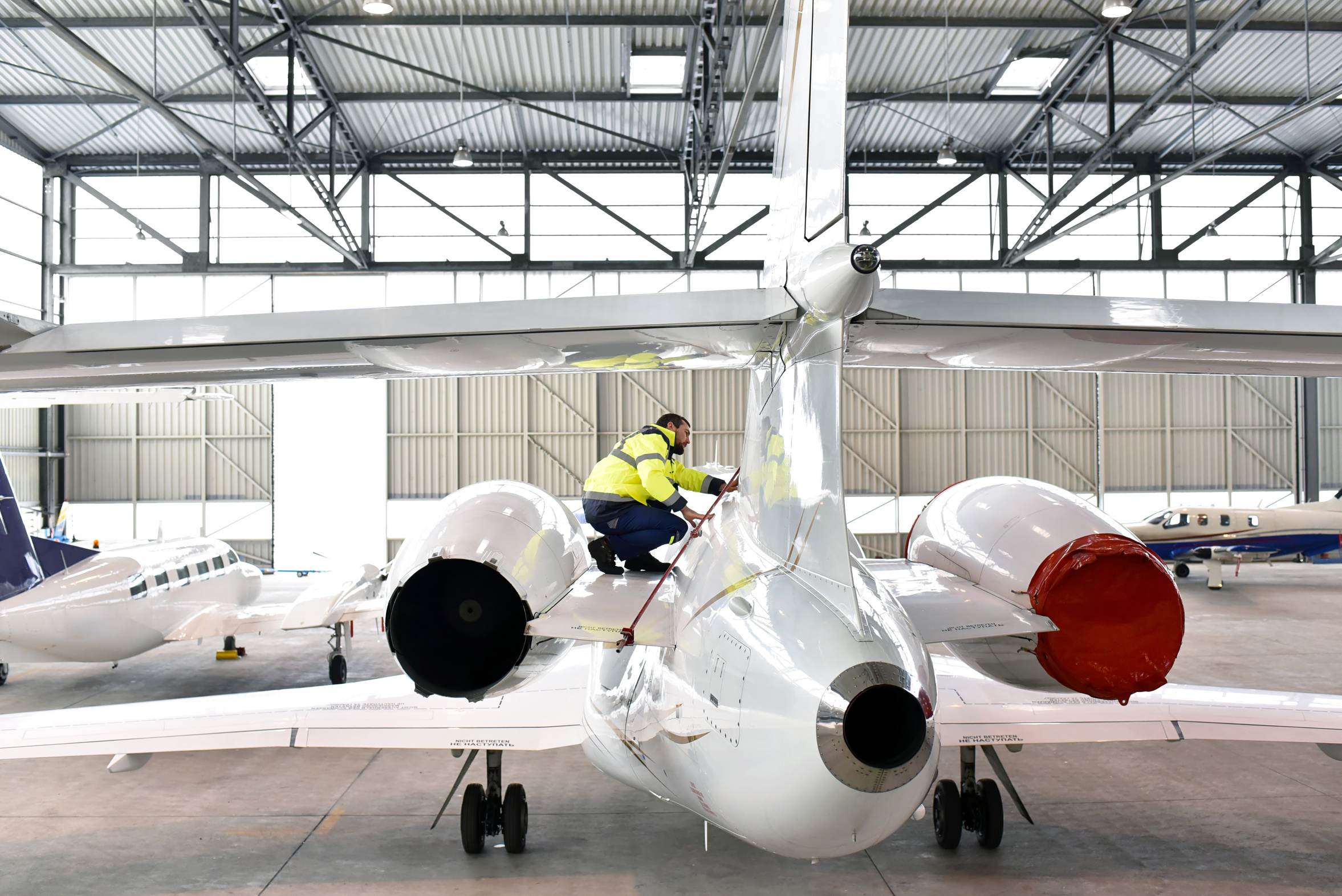 A technician working on a business jet in a bright maintenance hangar.