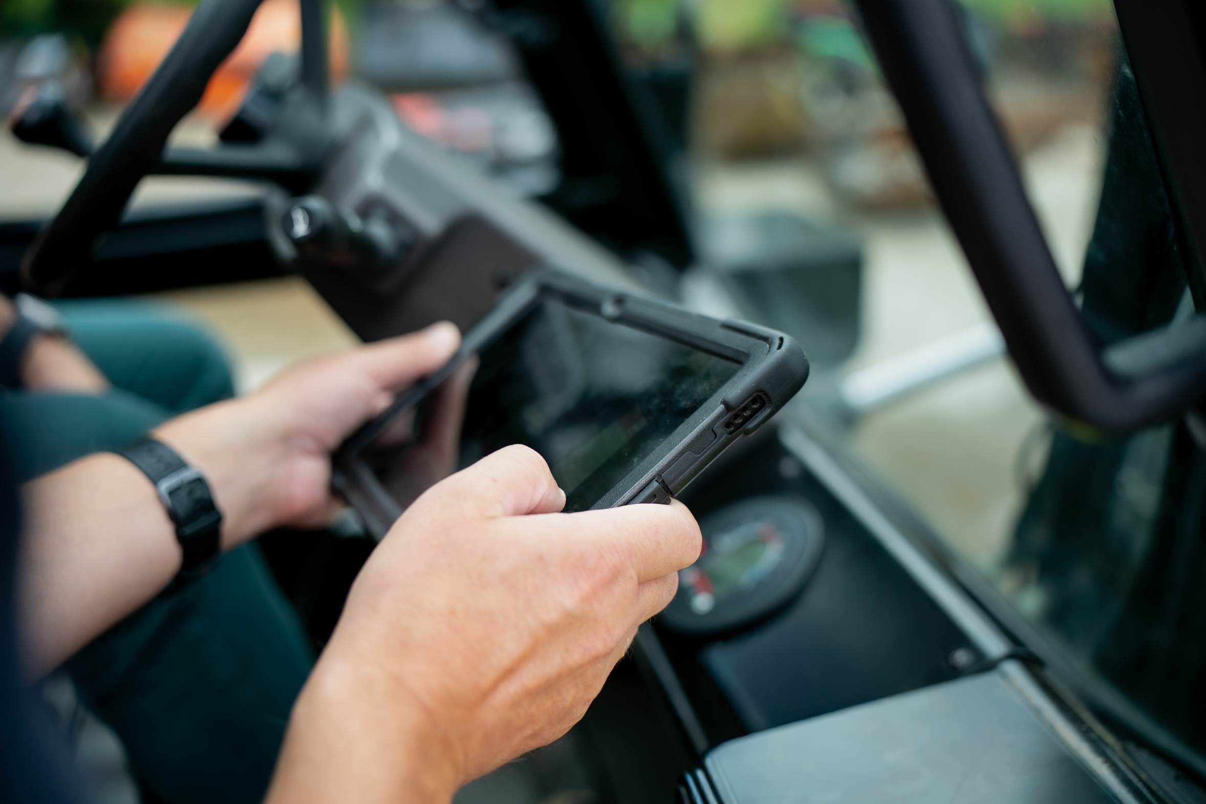 An operator's hands holding a tablet inside the cab of a heavy machine.